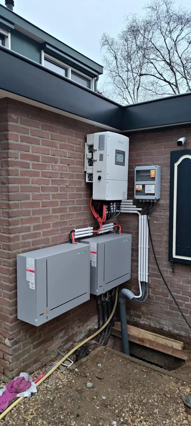 Echte buiteninstallatie aan een bakstenen gevel, met batterij, omvormer en bekabeling